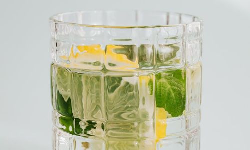 A glass of fresh water with a slice of lemon next to a window.